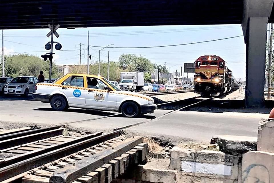 Como lo hacen otros automovilistas, un taxista se arriesga a pasar teniendo el tren a pocos metros en el cruce de Manuel L. Barragán y Juan Pablo II, en San Nicolás.