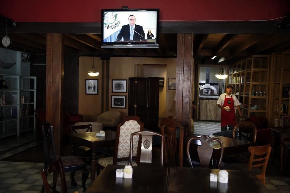 El Presidente guatemalteco, Alejandro Giammattei, aparece en un mensaje en televisión en un restaurante vacío.