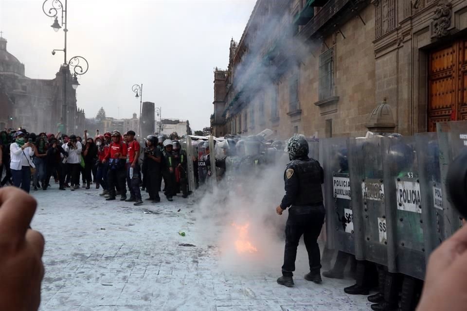 Policías que custodiaban la puerta Mariana del Palacio Nacional sofocan el fuego causado por una bomba molotov lanzada contra ellas durante la marcha del #8M.