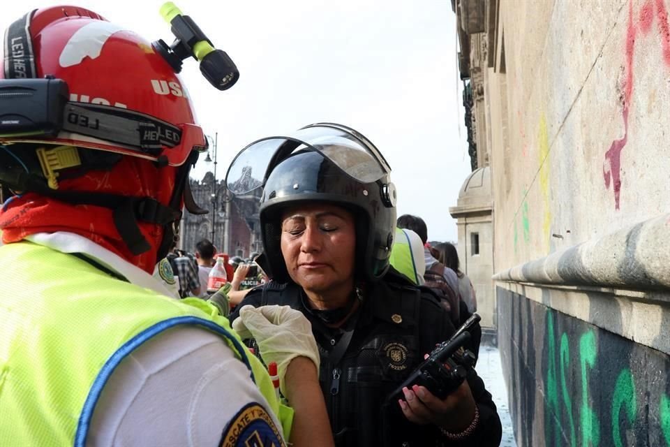 Una mujer mando de la Secretaría de Seguridad Ciudadana es asistida por un paramédico del ERUM, quien le limpia los ojos salpicados por vinagre lanzado en globos durante la marcha del #8M.