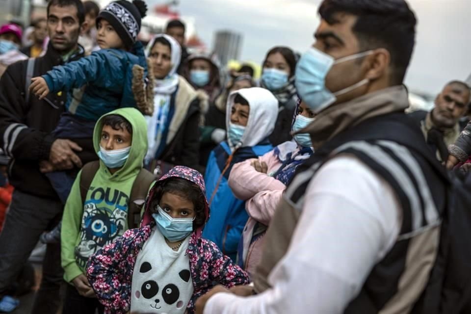 Migrantes y refugiados esperan con mascarillas un autobús cerca de Atenas, Grecia.