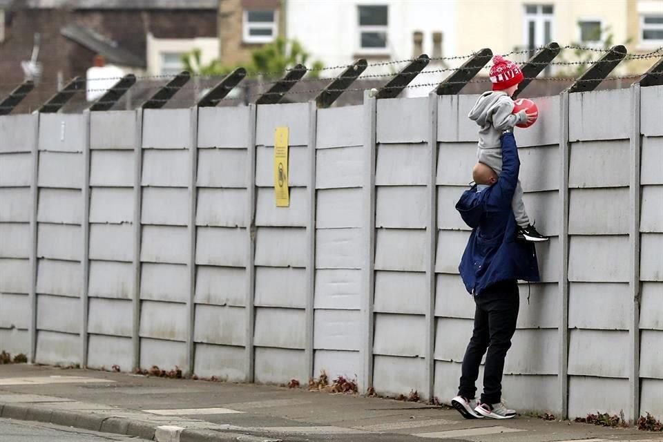Un hombre carga a un niño sobre sus hombros para que vea el entrenamiento del Liverpool, mientras el equipo entrenaba en grupos pequeños.