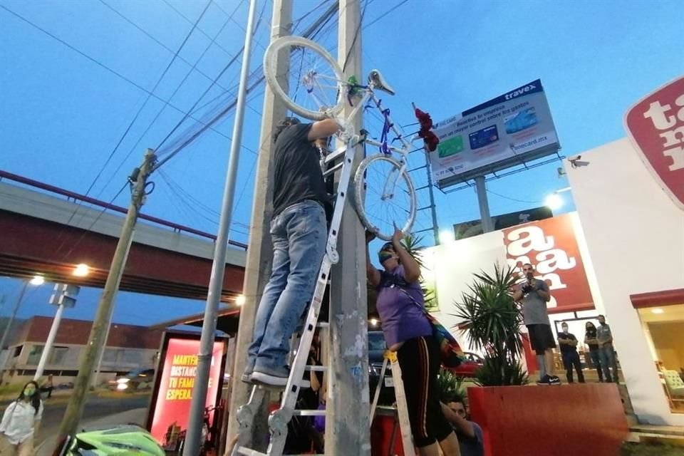 Tres personas del colectivo participaron en la instalación de una bicicleta blanca en un poste de luz. 