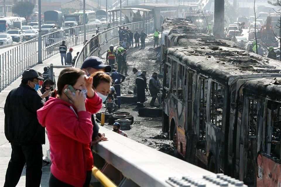 Ciudadanos observan hoy los restos incinerados de buses de TransMilenio en la localidad de Bosa, en Bogotá.