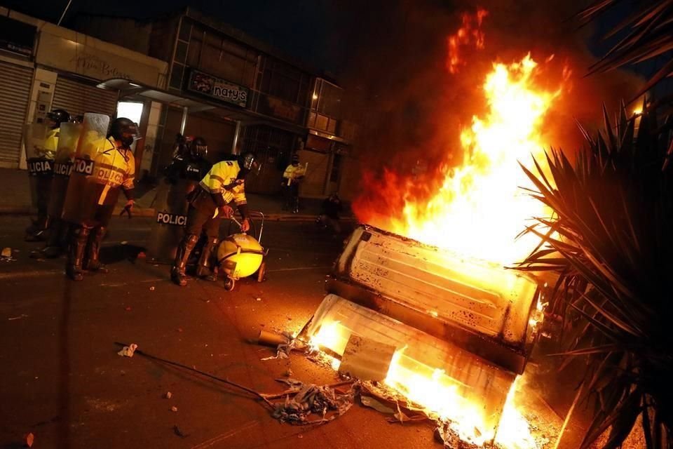 Miembros de la policía pasan junto a un cubo de basura ardiendo el jueves por la noche, durante una protesta contra la violencia policial, en Bogotá.