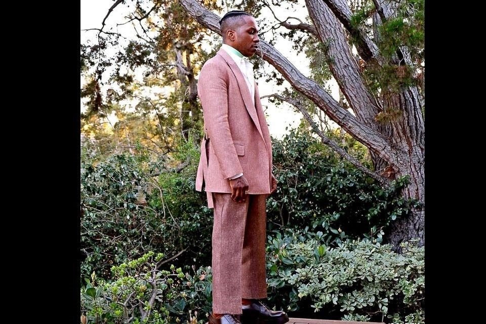 Leslie Odom Jr. apostó por un traje casual en tonos salmón, camisa rosa y suéter con cuello alto en neón de la firma española Loewe.