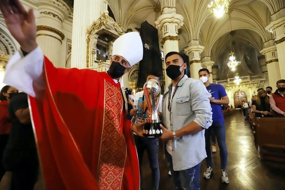 Aldo Rocha sostiene el trofeo de campeón junto al sacerdote que oficio ayer la misa.
