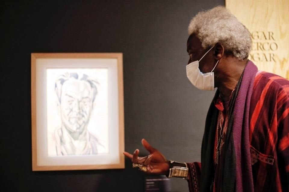 El curador de la exposición, Ery Camara, junto a un autorretrato del artista.
