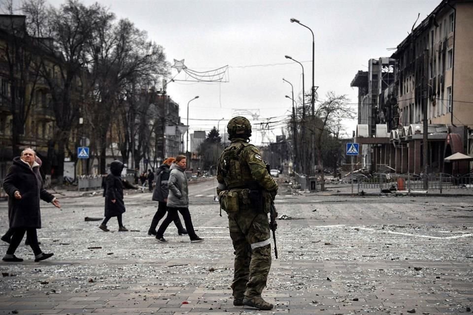 Personas caminan el martes por las calles de Mariúpol cerca de un soldado ruso.