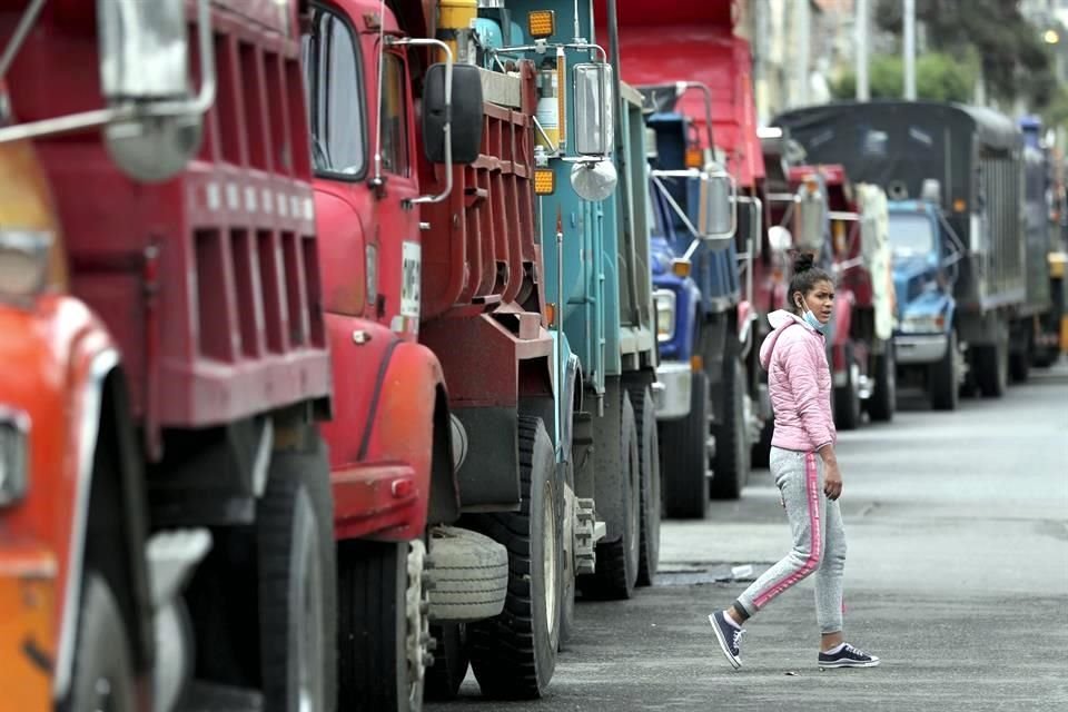 Una mujer camina frente a camiones de basura que pararon por la huelga en Colombia.