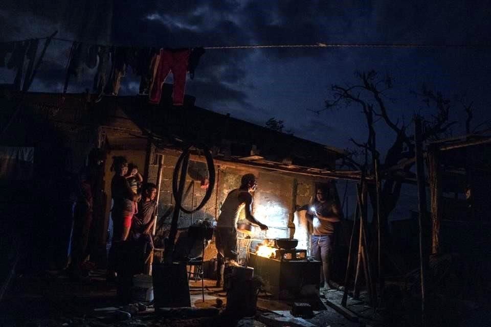 Una familia prepara la cena  afuera de su casa dañada por la tormenta 'Ian' que los dejó sin electricidad.