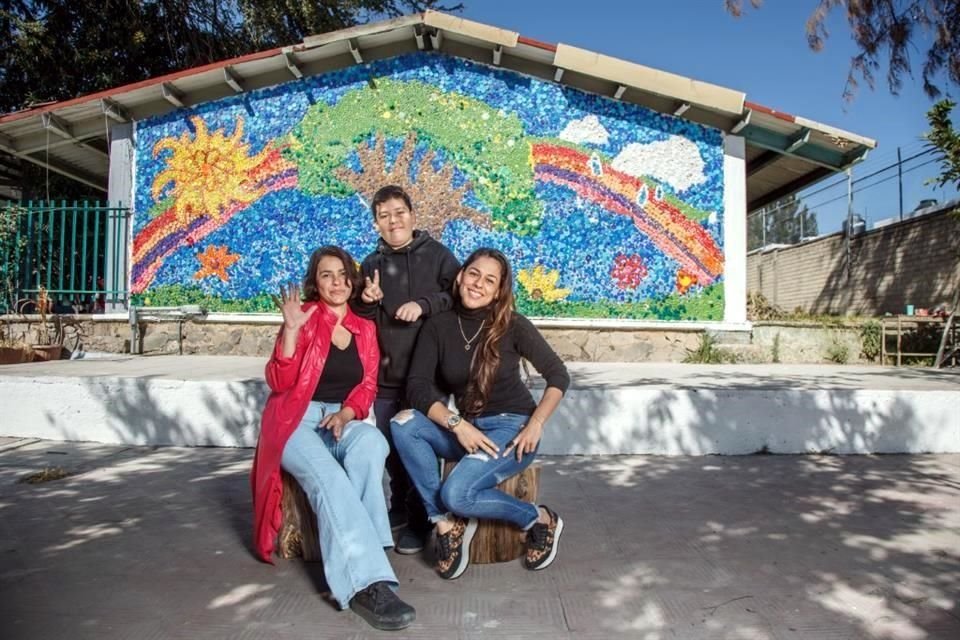 Jeremy Francisco Ortiz, Fedra Mimendi Orozco (blusa negra) y Angélica Barba (rojo) posan frente al mural hecho con tapitas.