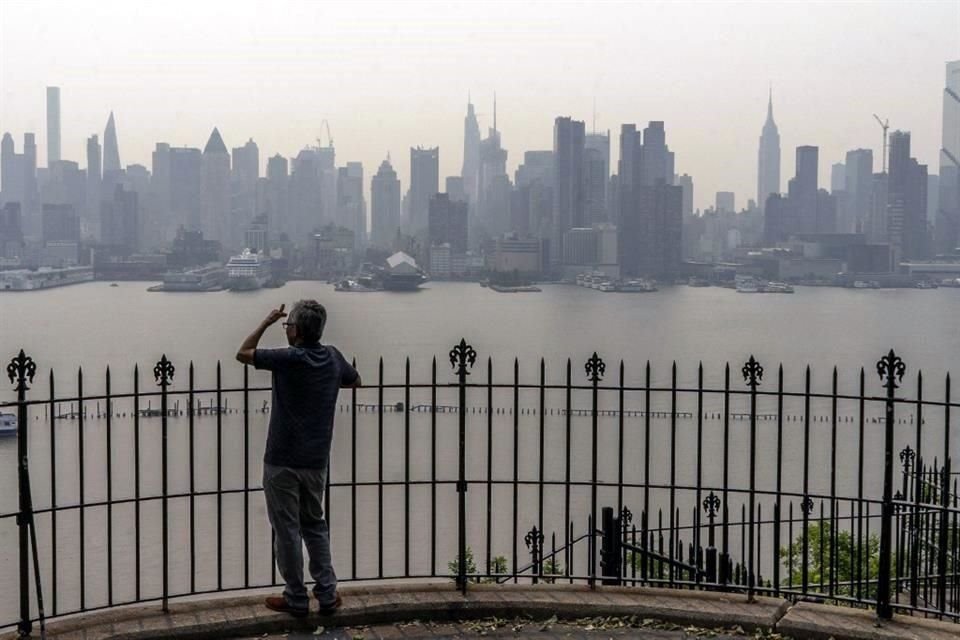 Una persona mira el horizonte de la ciudad de Nueva York mientras está cubierto de neblina y humo de los incendios forestales de Canadá.