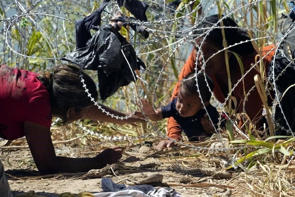 Dos mujeres intentan pasar a un niño entre un alambre de púas en la frontera de Estados Unidos con México.