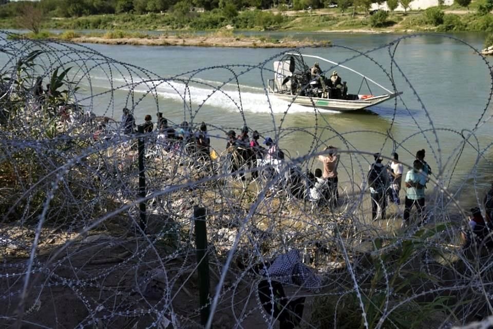 Elementos de la Patrulla Fronteriza pasan en una lancha frente a decenas de migrantes.