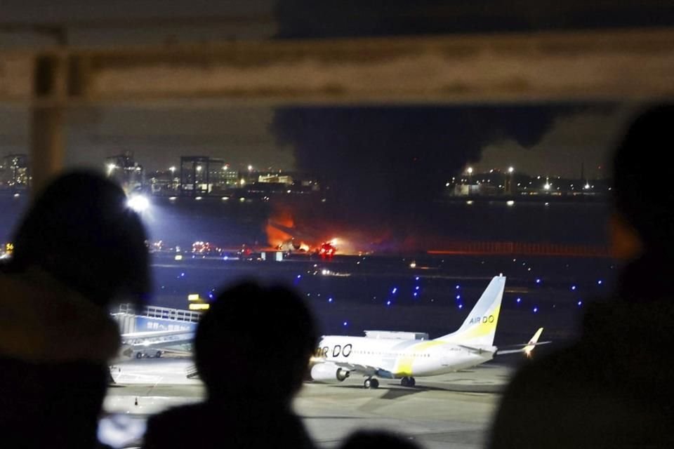 La gente observa cómo se incendia un avión de Japan Airlines en la pista del aeropuerto de Haneda.