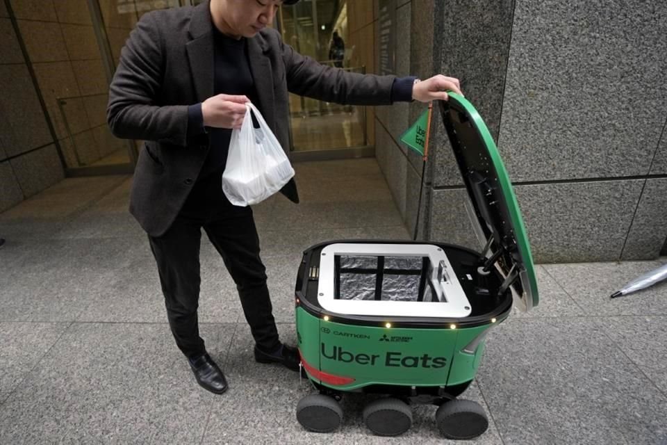 Una persona recibe su pedido desde el contenedor de un robot de entrega de alimentos Uber Eats durante su demostración para los medios en Tokio, Japón.