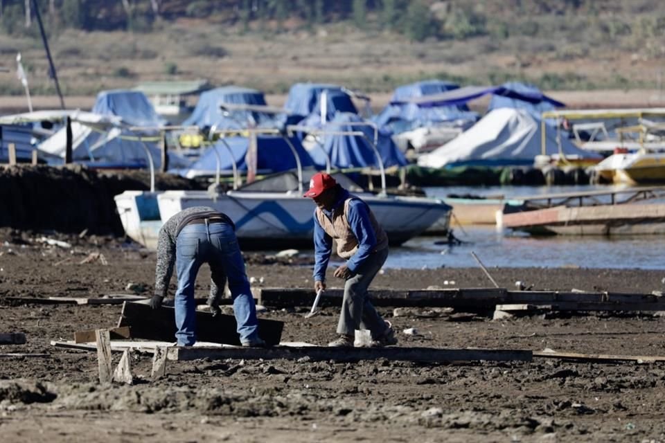 Lancheros que trabajan en la presa Miguel Alemán han hecho un camino de tablas y piedras en las zonas donde ha bajado el nivel del agua.