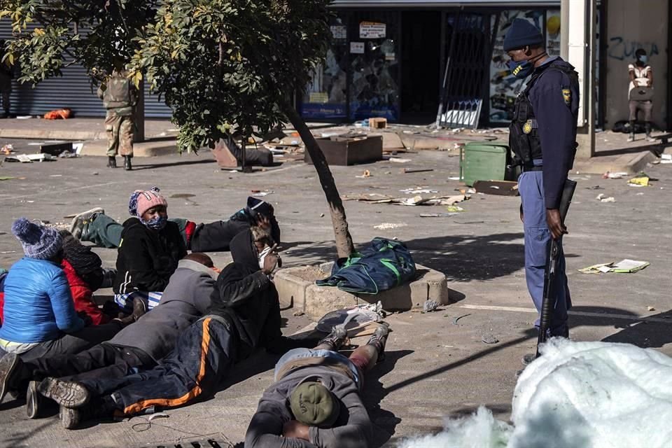 Un policía vigila a un grupo de personas arrestadas durante un intento de saqueo en Sudáfrica.