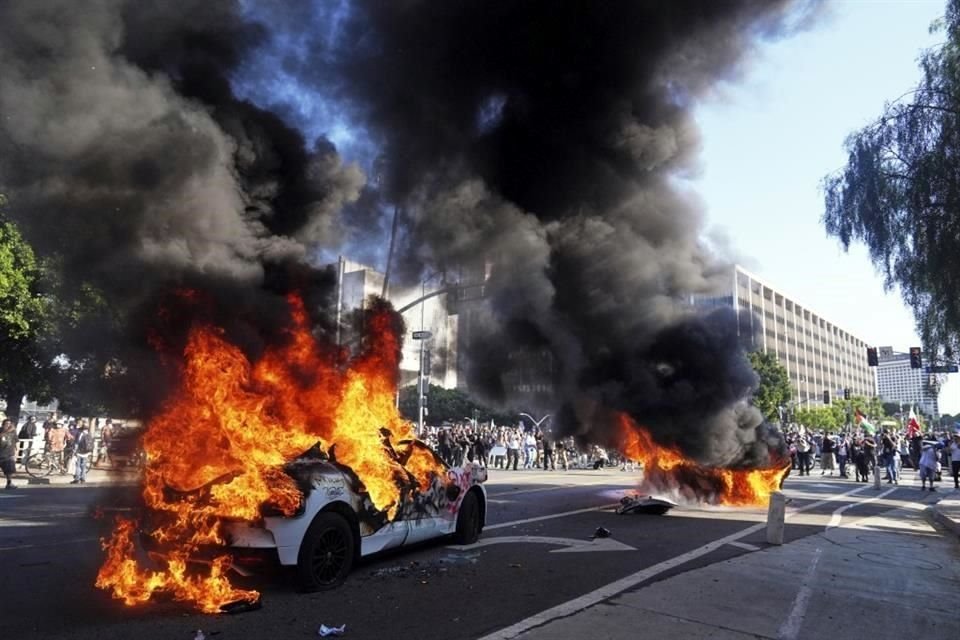 Aspecto de dos taxis ardiendo, después de los enfrentamientos entre manifestantes y agentes policiacos en las inmediaciones del Centro de Detenciones de Los Angeles.