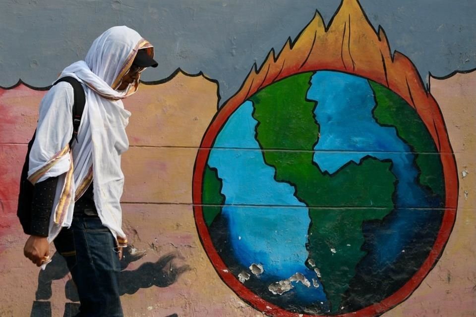 Un hombre se cubre la cara del calor mientras camina junto a un mural en Varanasi, el 9 de junio.