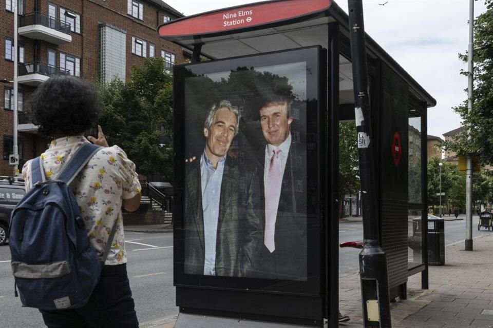 Pasajeros pasan junto a una parada de autobús cerca de la estación Nine Elms mientras activistas colocan un cartel que muestra al Presidente Donald Trump y a Jeffrey Epstein.