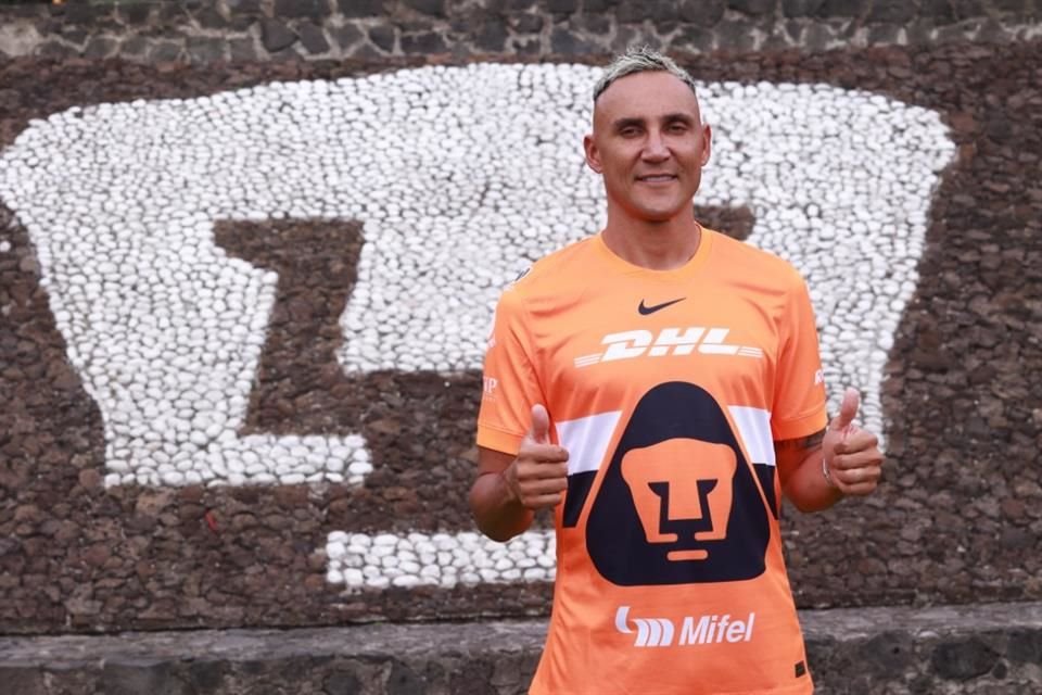 Keylor Navas posa con el uniforme de Pumas y al fondo el escudo de la institución.