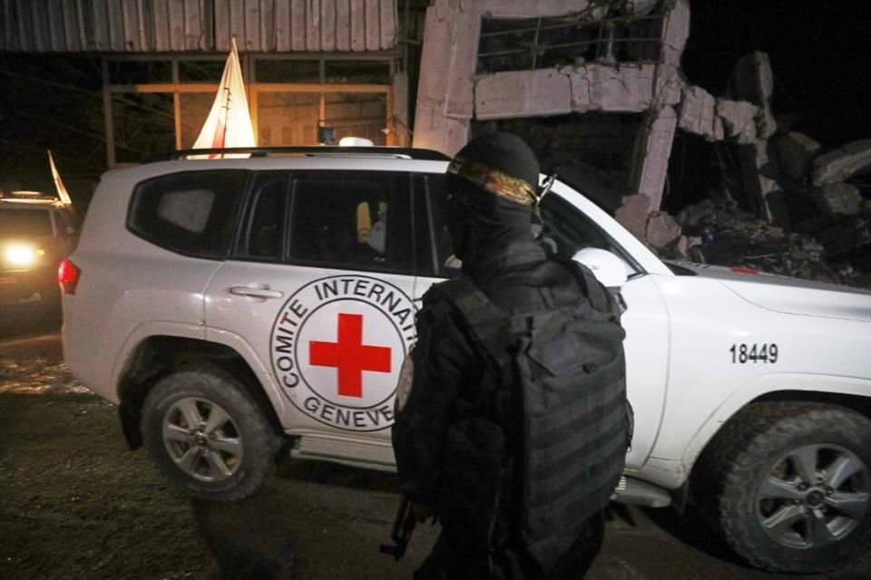 Un hombre armado que viste el uniforme de las Brigadas al-Qassam, el ala militar de Hamás, hace guardia mientras los vehículos de la Cruz Roja transportan ataúdes con cuatro rehenes fallecidos.