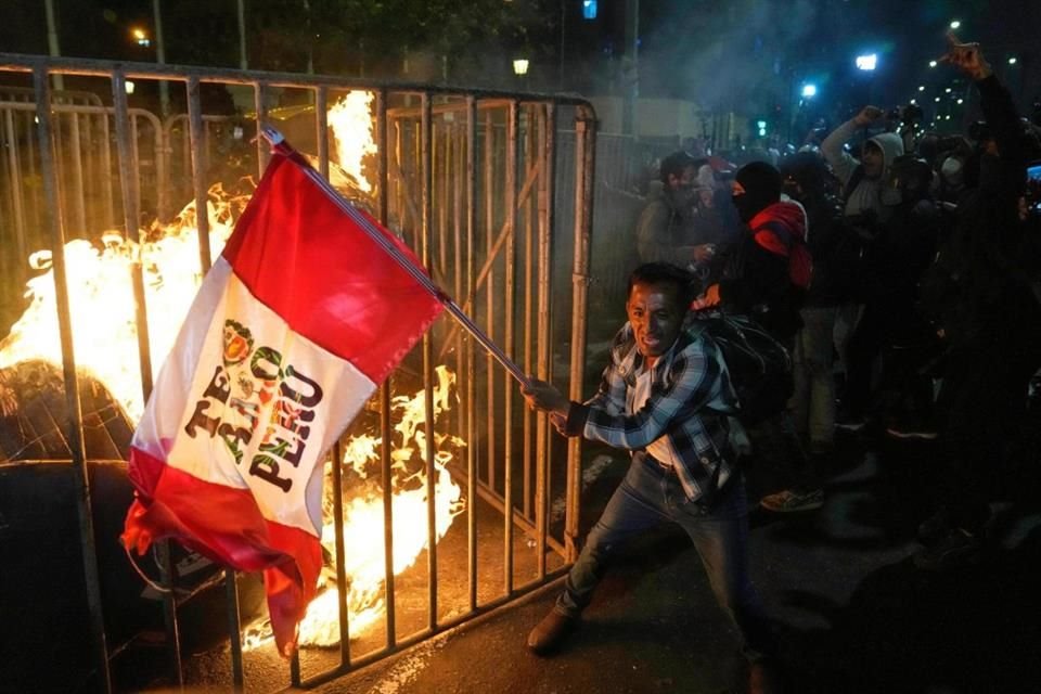 Un manifestante ondea una bandera peruana mientras una muñeca de cartón arde frente al Congreso durante una protesta en Lima, el 15 de octubre de 2025.